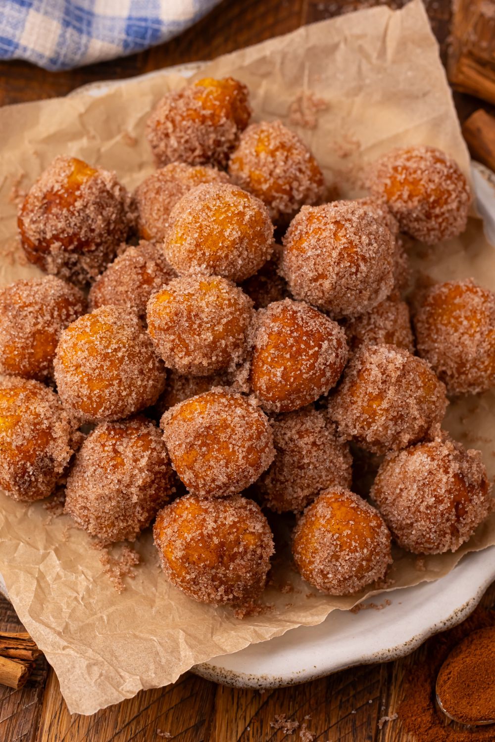 Wooden table with a white platter full of a stack of Pumpkin Pie Donut Holes that are rolled in cinnamon and sugar 