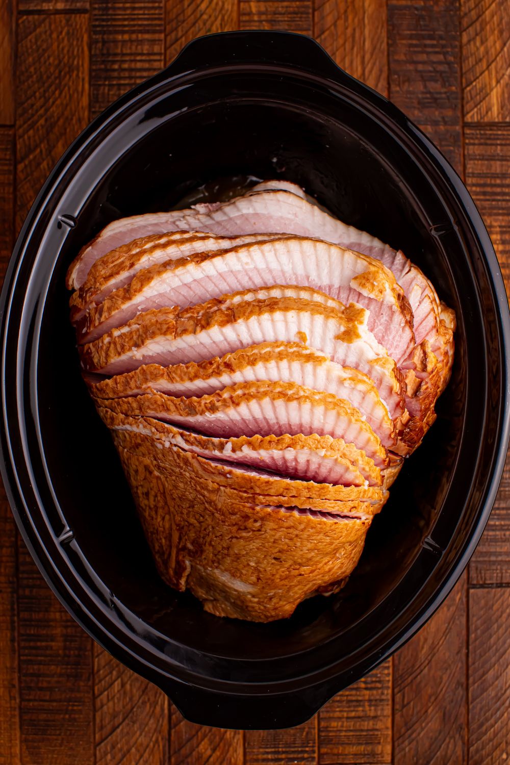 raw spiral cut ham sitting on a wooden table in a black slow cooker