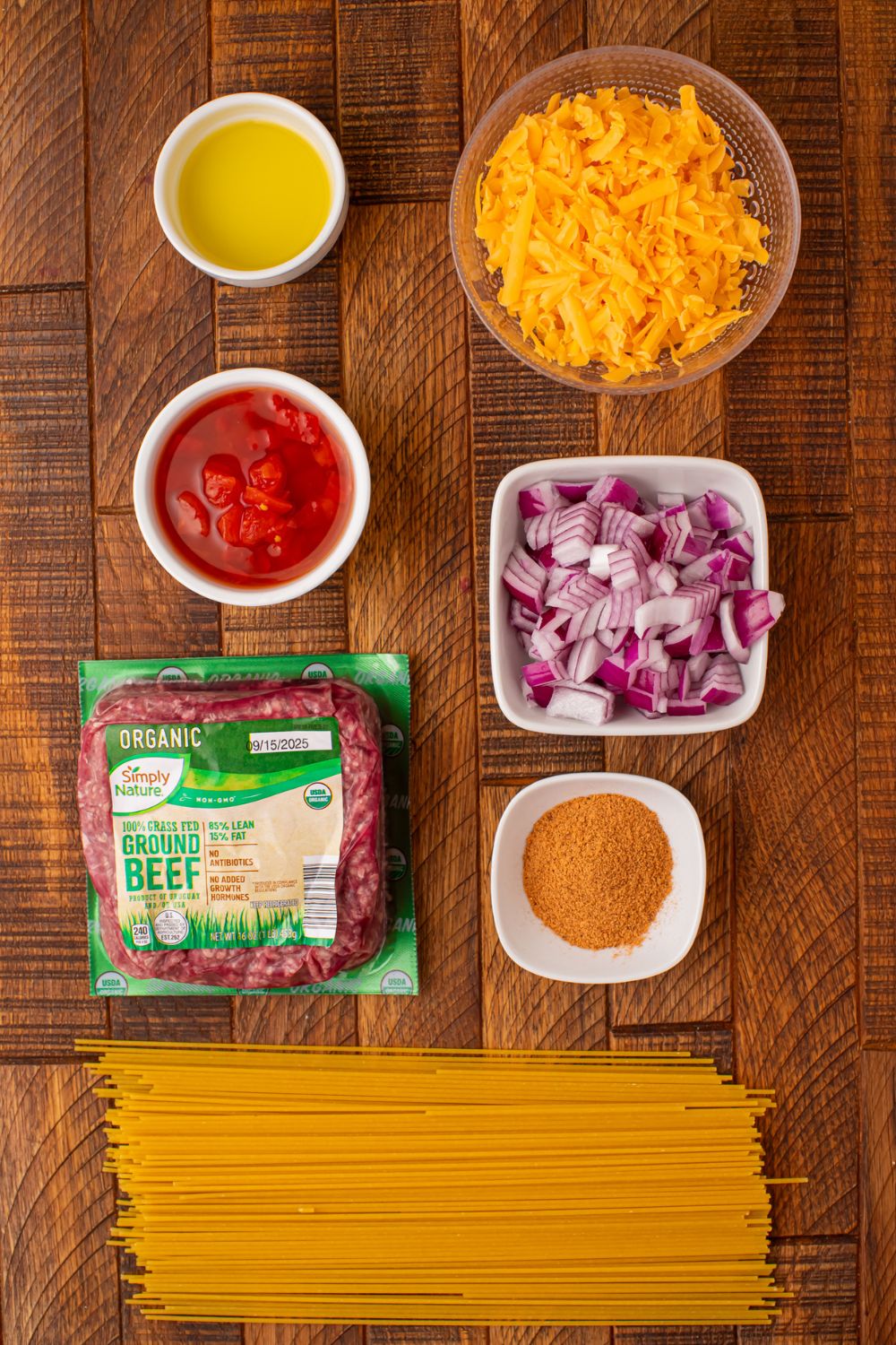 a wooden table full of items to make taco spaghetti in single serve small bowls. 