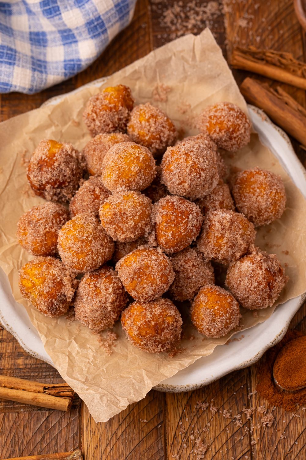 Pumpkin Pie Donut Holes  on a white plate with parchment paper under the donut holes with a blue checkered towel behind it 