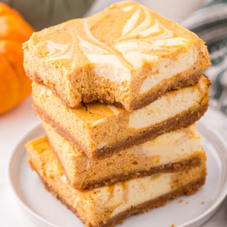 Sliced Swirled Pumpkin Cheesecake Bars stacked on a whit platw