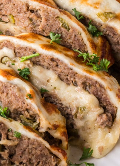 Stuffed Philly Cheesesteak Meatloaf on a white platter on wooden table that is partly sliced and ready to serve