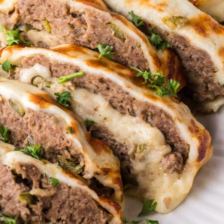 Stuffed Philly Cheesesteak Meatloaf on a white platter on wooden table that is partly sliced and ready to serve