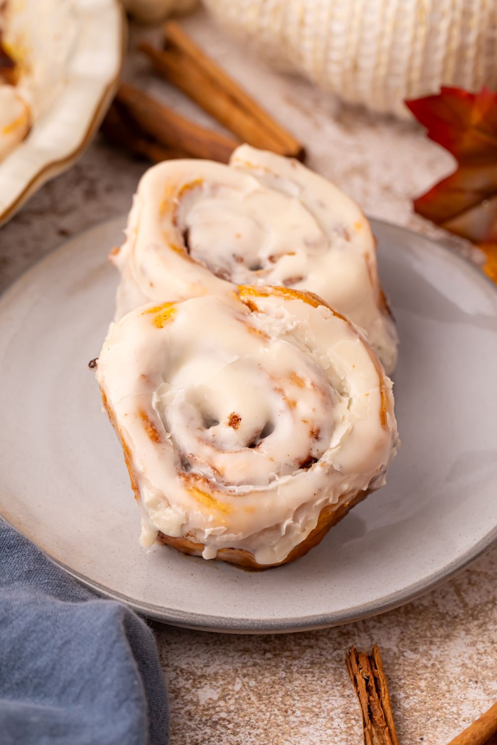 2 Pumpkin Cinnamon Rolls on a plate with cinnamon sticks, pumpkins and more fall themed items decorated around table
