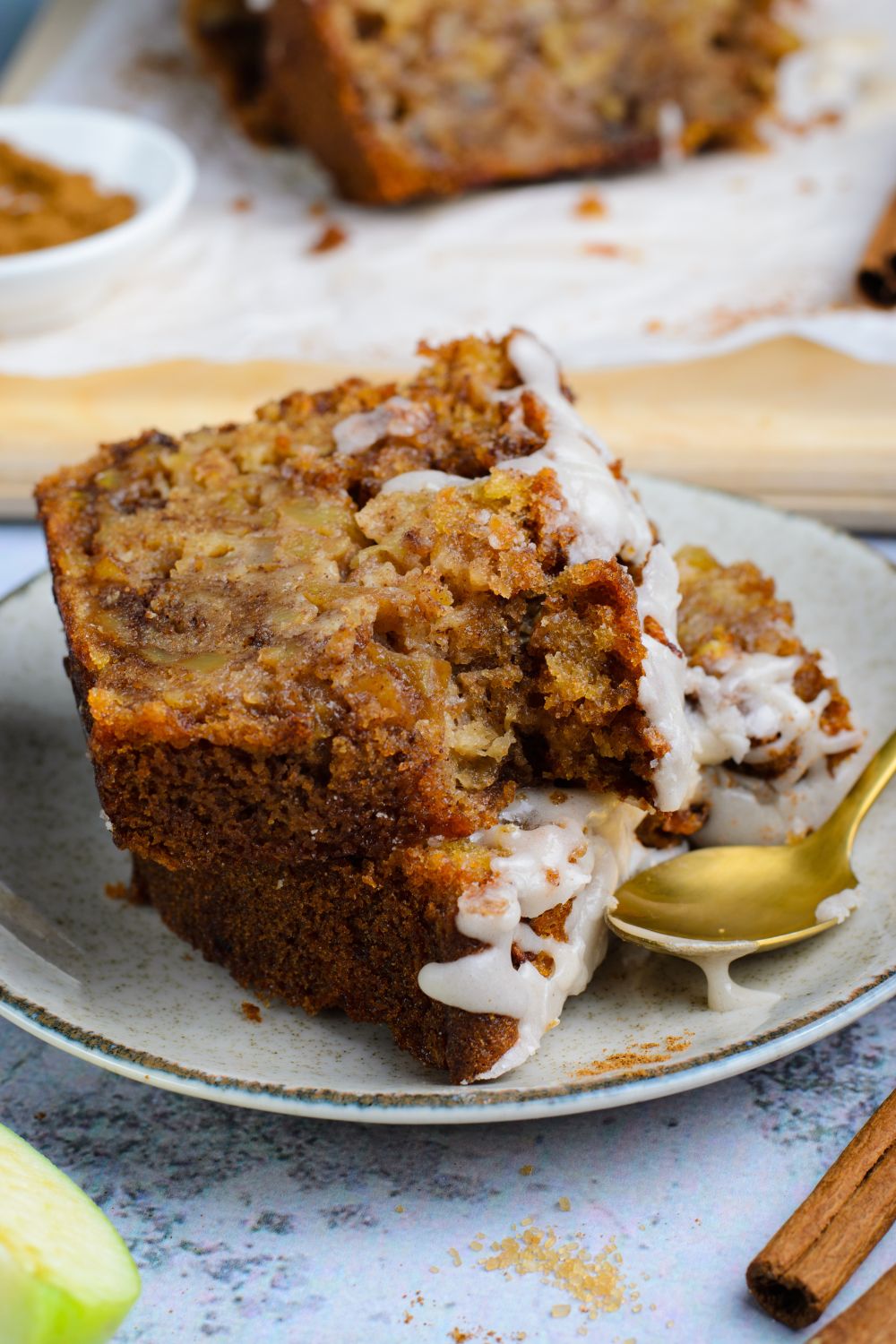 two slices of Amish Apple Fritter Bread  on a white plate with a gold spoon to side showing a couple bites taken out of it 