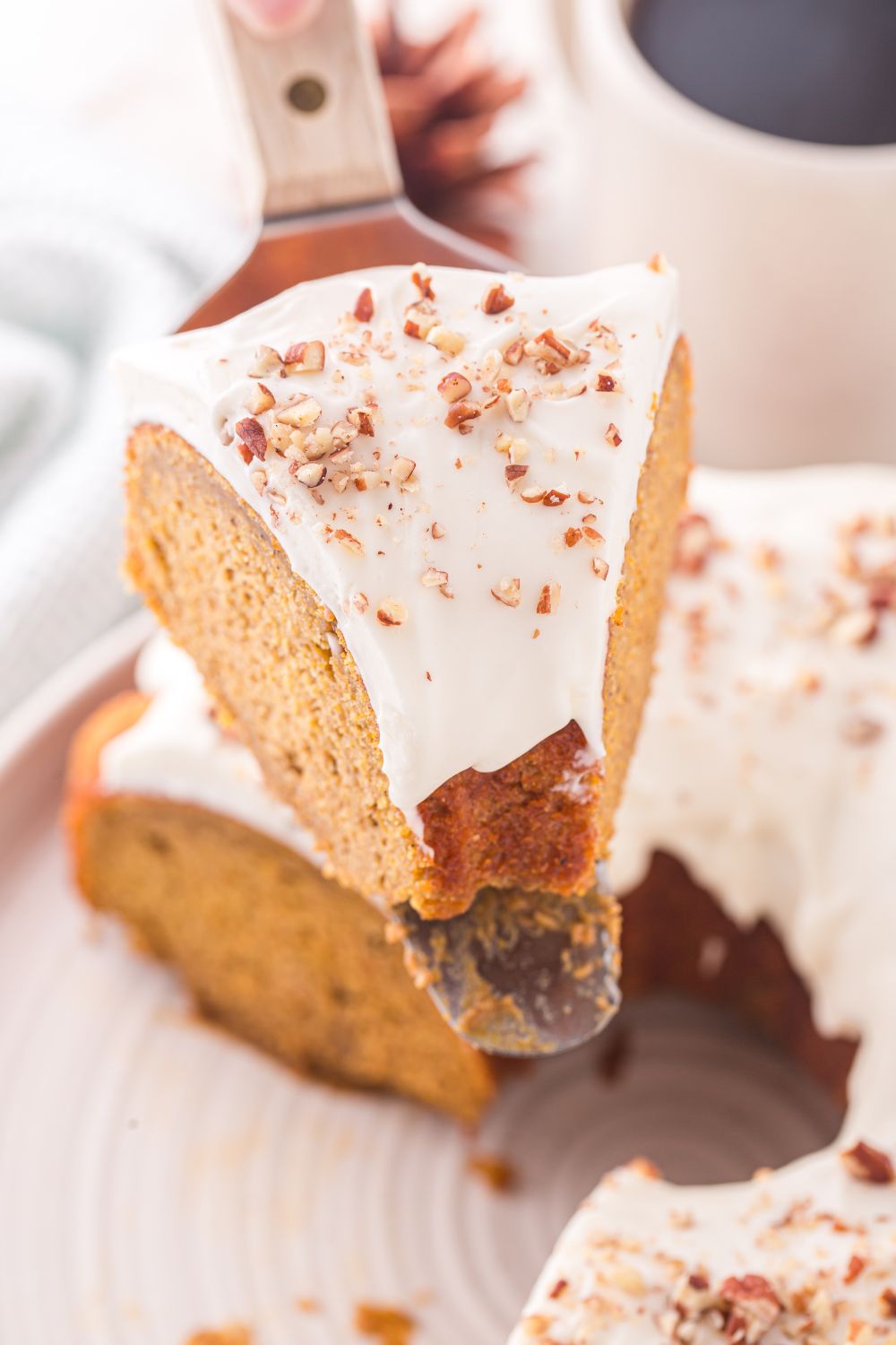 Pumpkin Bundt Cake on spatula above rest of cake on a white cake platter on table 
