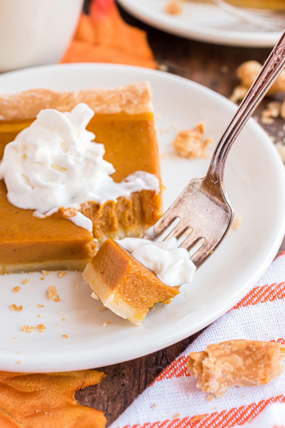 slice of Sheet Pan Pumpkin Pie on a white plate with a fork with a biteful on it. Then a towel to side on a wooden table 