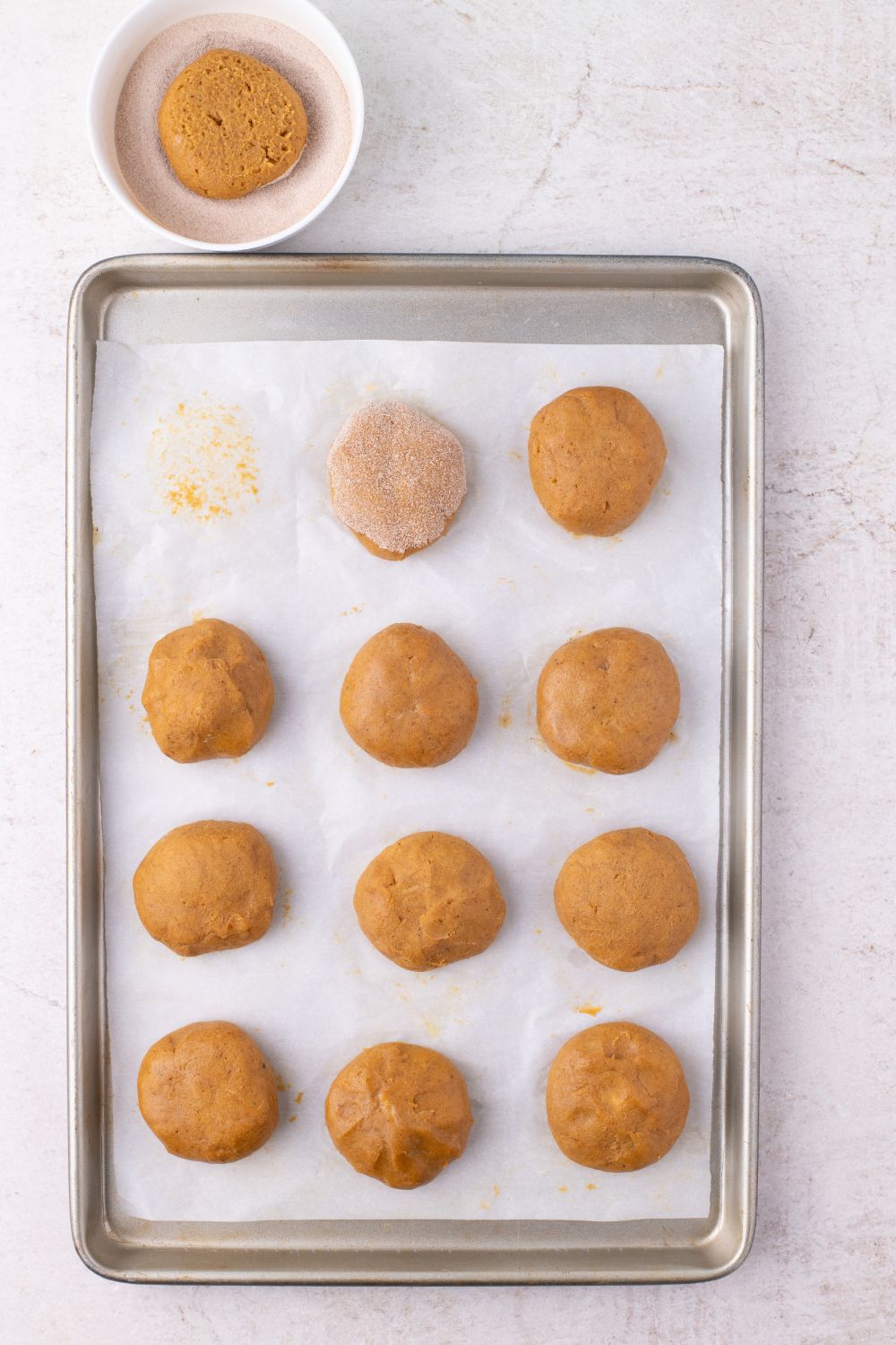 raw pumpkin cookie dough on baking sheet with cinnamon sugar coating on cookie balls 