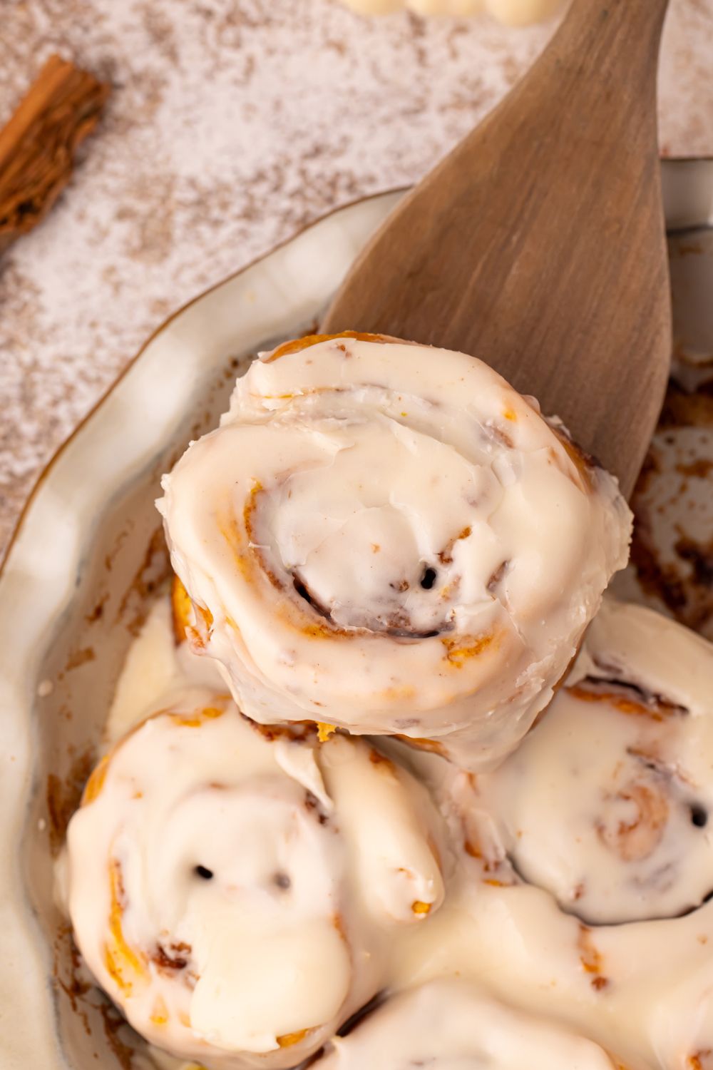 Pumpkin Cinnamon Rolls in a pie plate on table with a wooden spatula scooping one out of the pan