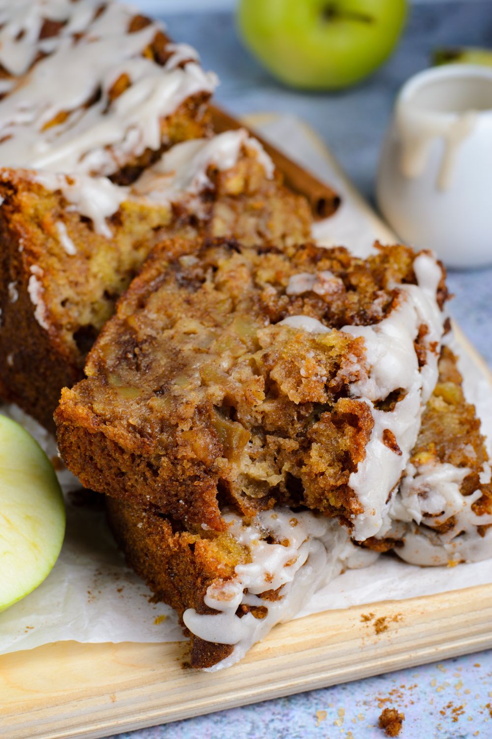 Apple bread with real apples sliced and placed on table with a bite taken out of the top slice of bread and apples around it on table for decor 