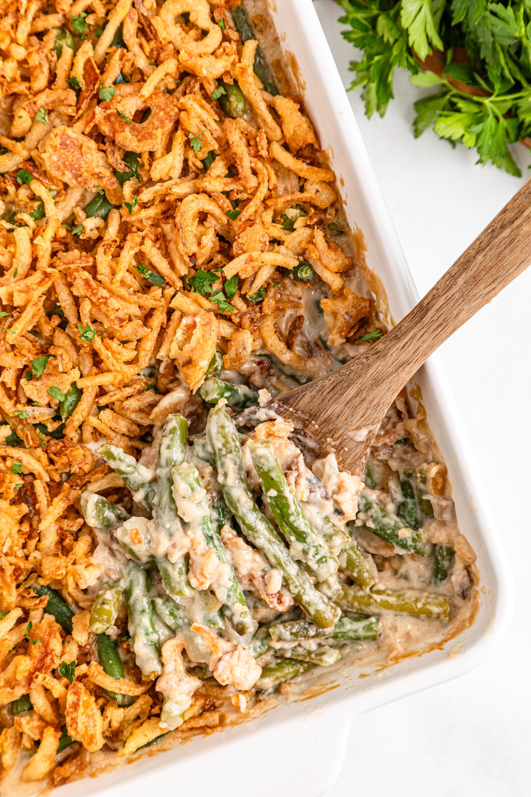 Best Ever Green Bean Casserole in a white baking dish with a spoon scooping some out 