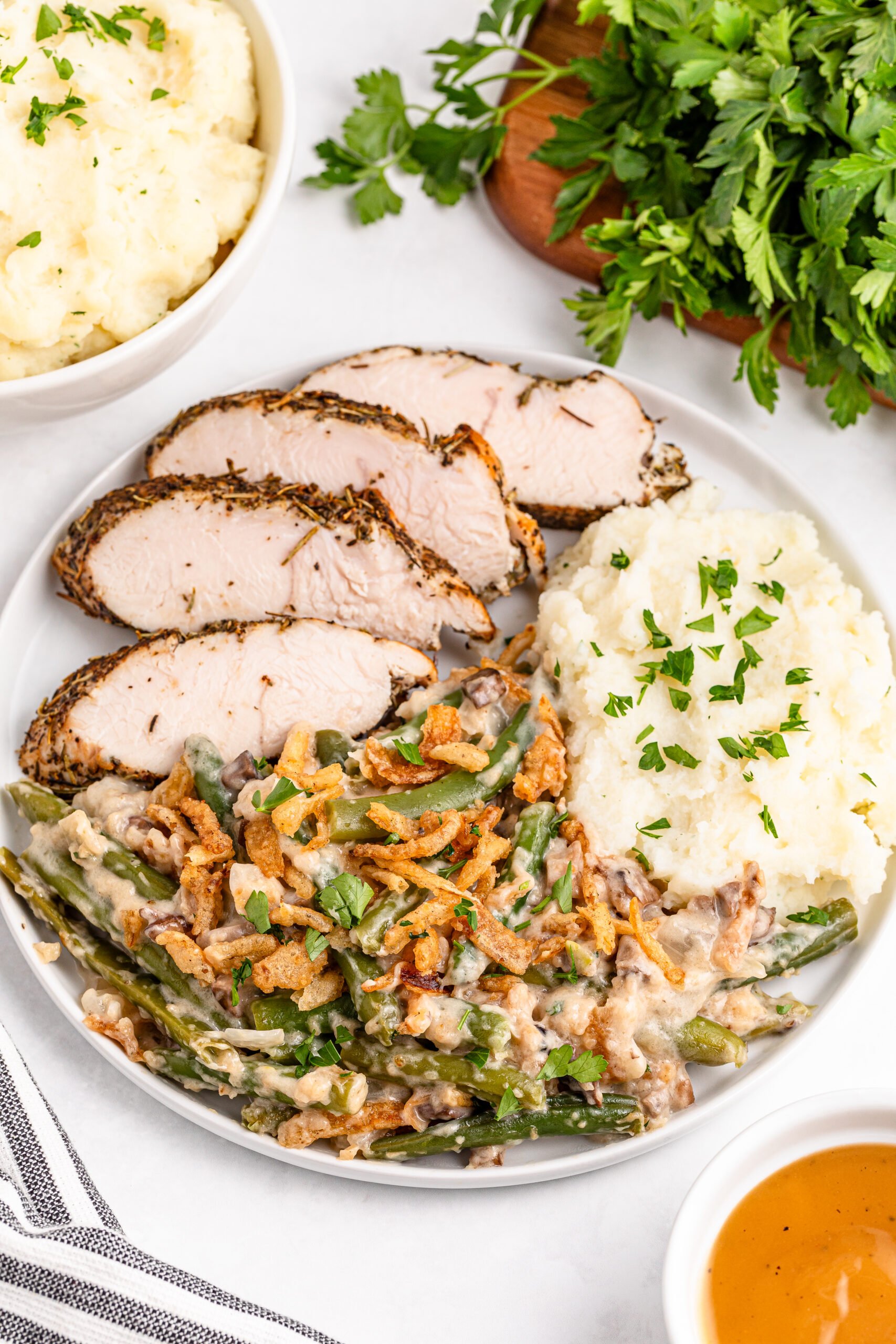 Green bean casserole on a white plate along side mashed potatoes and sliced turkey 