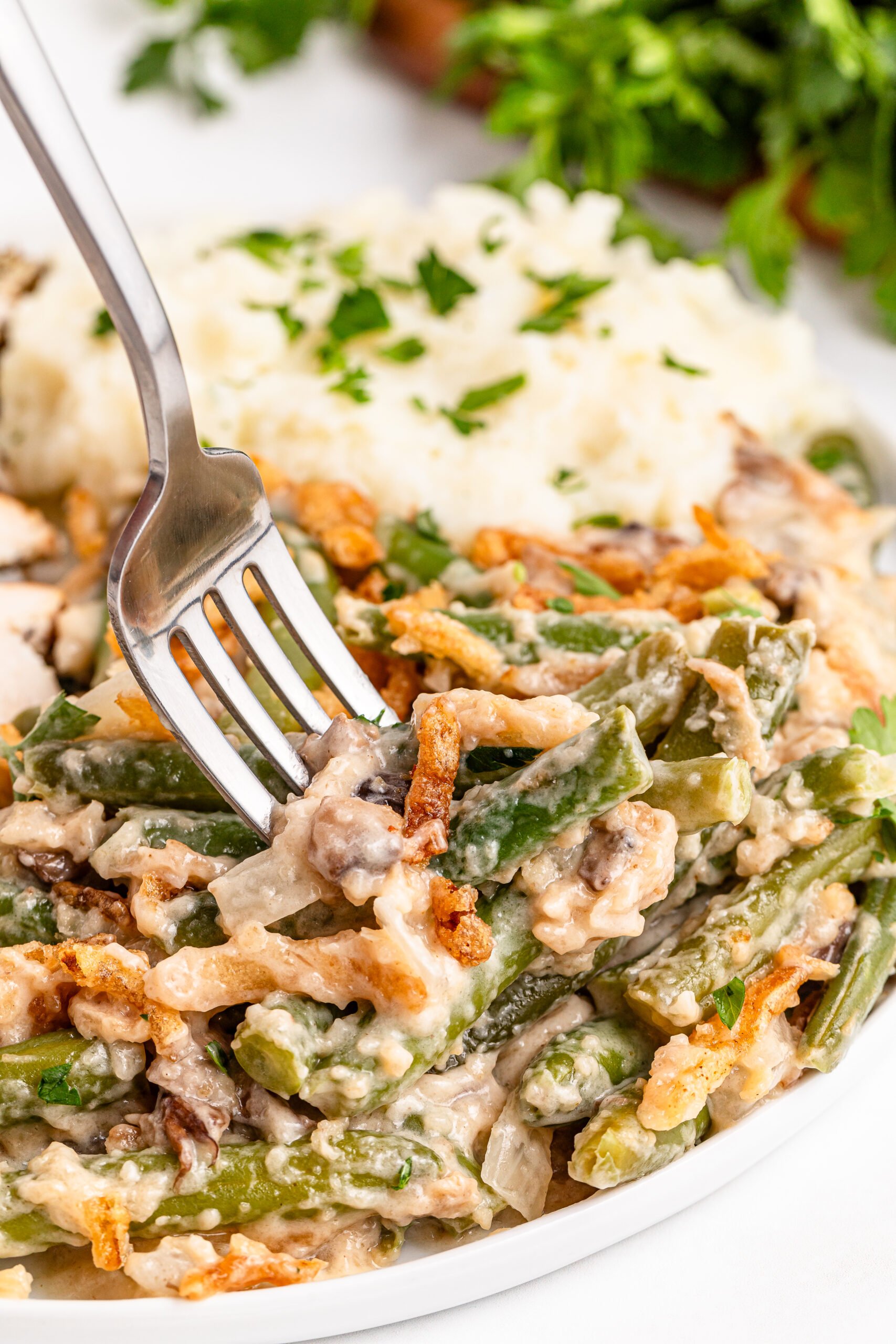 a fork going in for a bite of the Best Ever Green Bean Casserole in a white plate