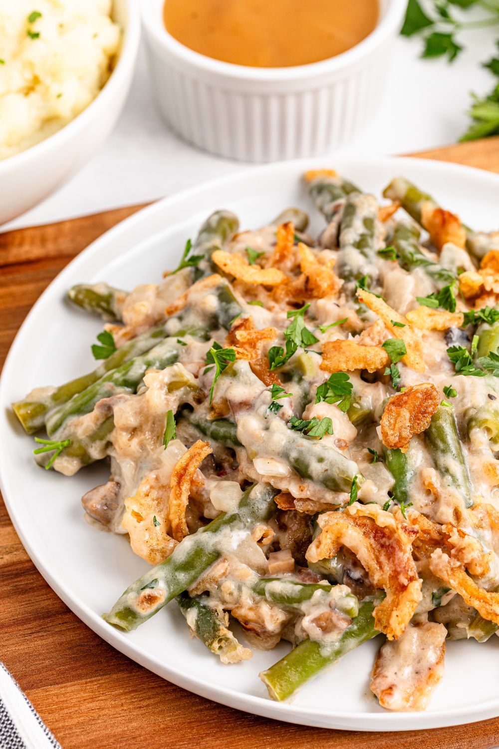 white plate sitting on table full of Green Bean Casserole. A brown towel is under the plate on table 