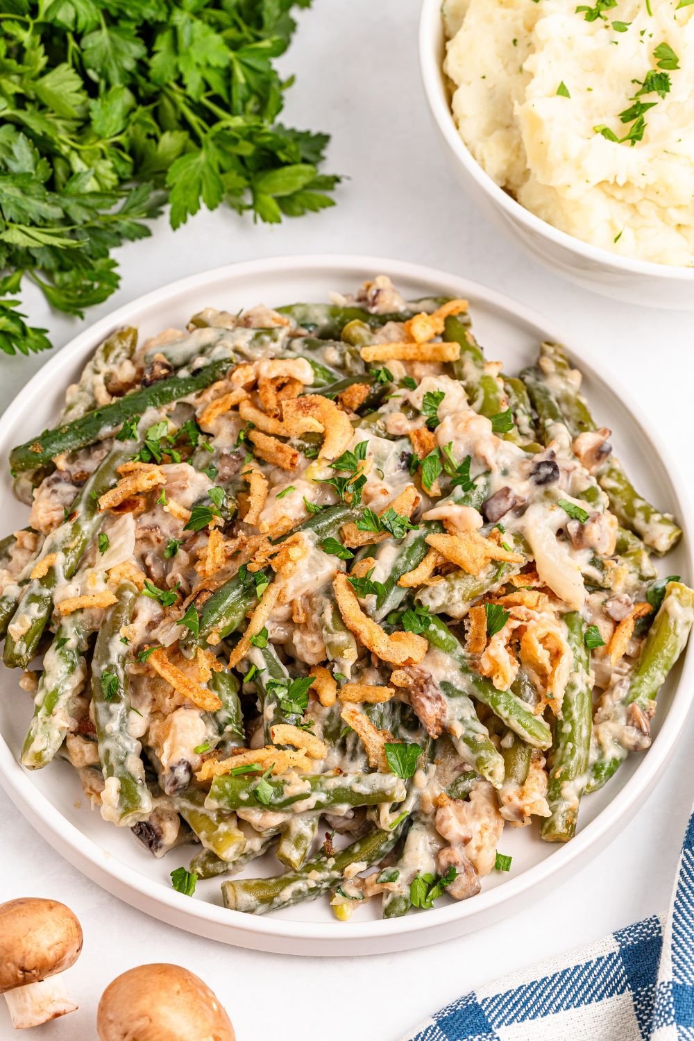 round white plate full of Green Bean Casserole with some fresh mushrooms to side on table, and fresh parsley