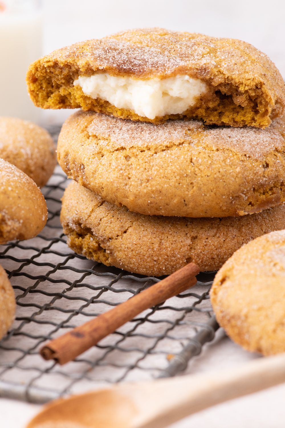 Pumpkin Cheesecake Cookies stacked on a cooling rack on table with a cinnamon stick and wooden spoon  in front 