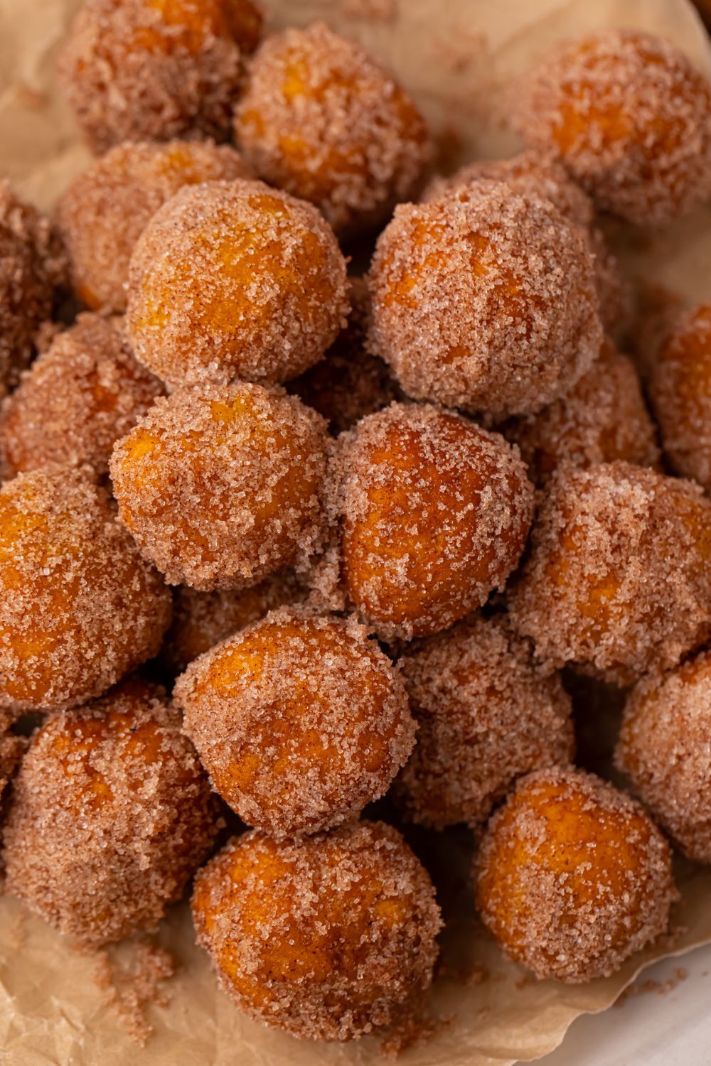 a stack of Pumpkin Pie Donut Holes rolled in cinnamon and sugar coating with parchment paper under the donut holes 