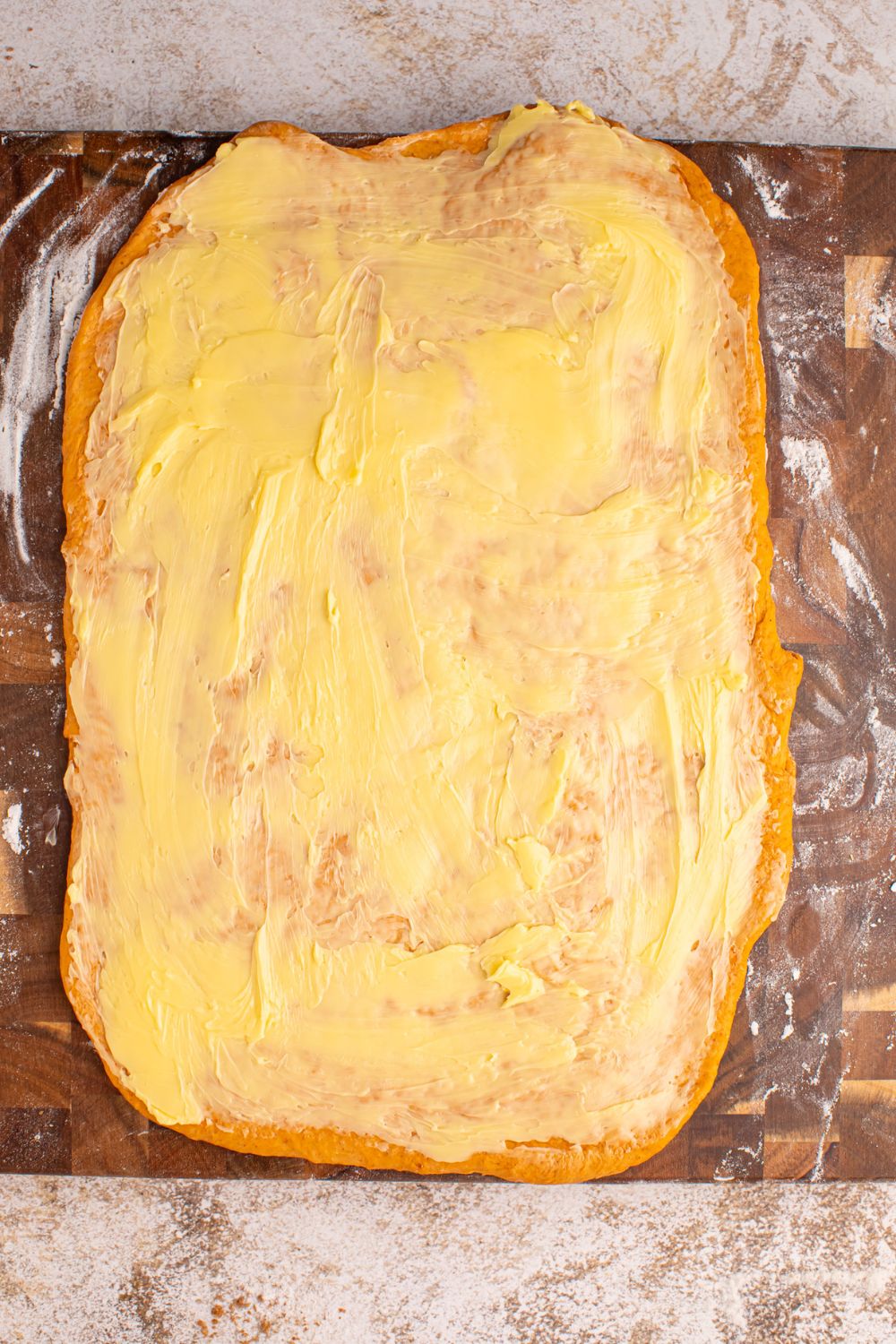 Pumpkin Cinnamon Roll dough spread out with a slather of butter all over the dough 