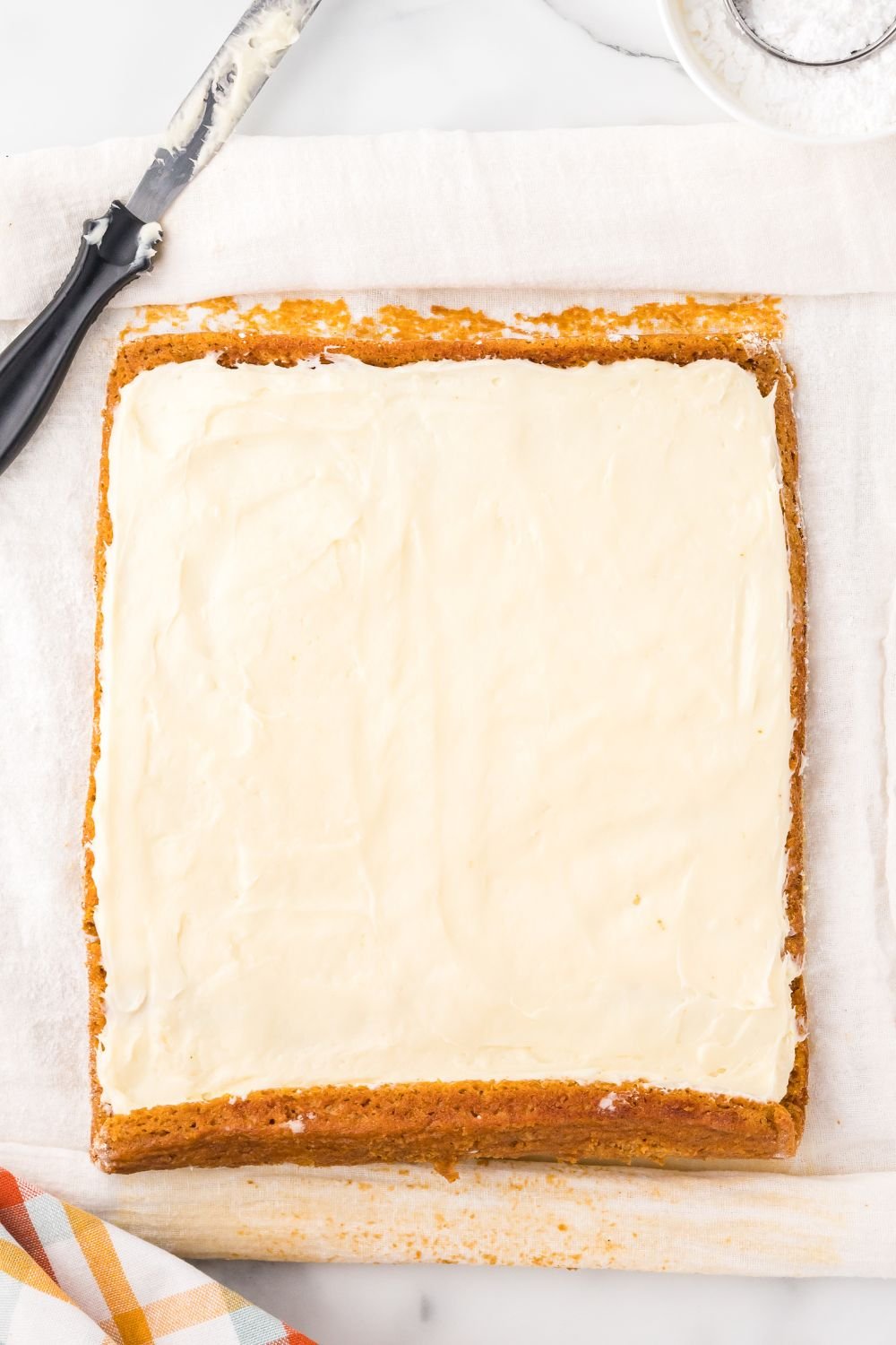 pumpkin roll laid out on marble counter spread with cream cheese filling all over