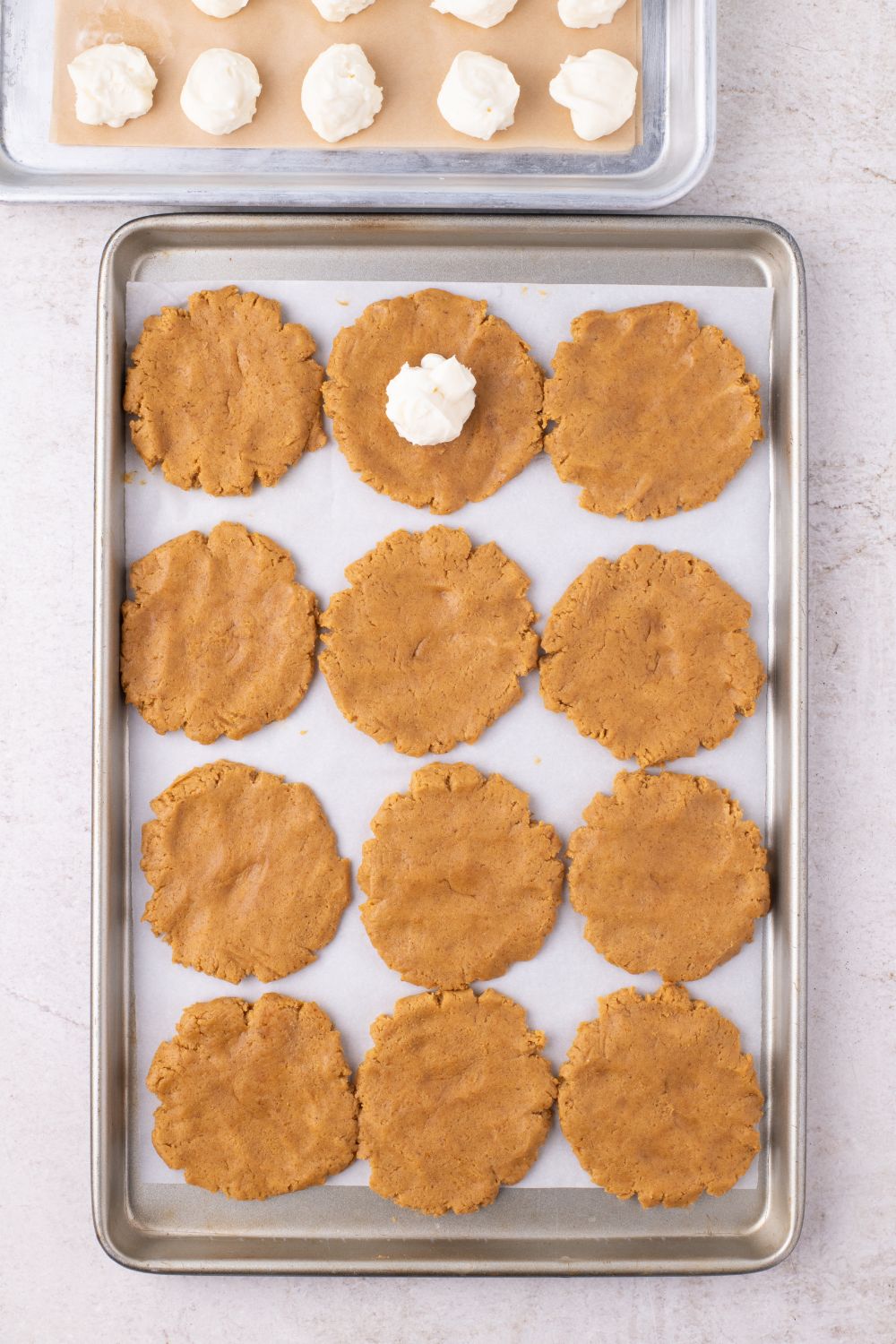 flat raw cookie dough on baking tray for cookies with a cheesecake batter in center of one of the cookies 