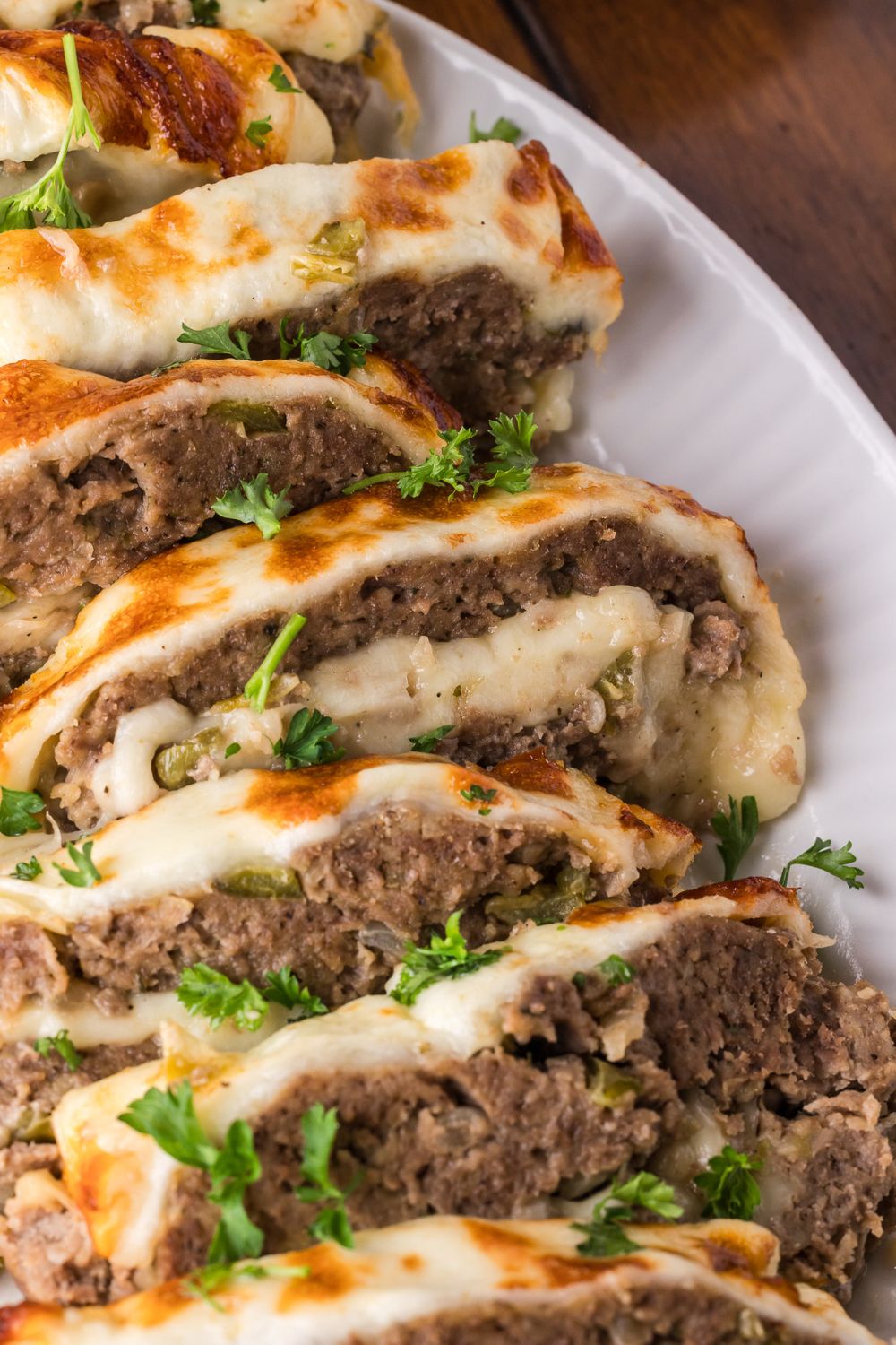 a white plate on wooden table with sliced Stuffed Philly Cheesesteak Meatloaf on plate topped with chopped parsley