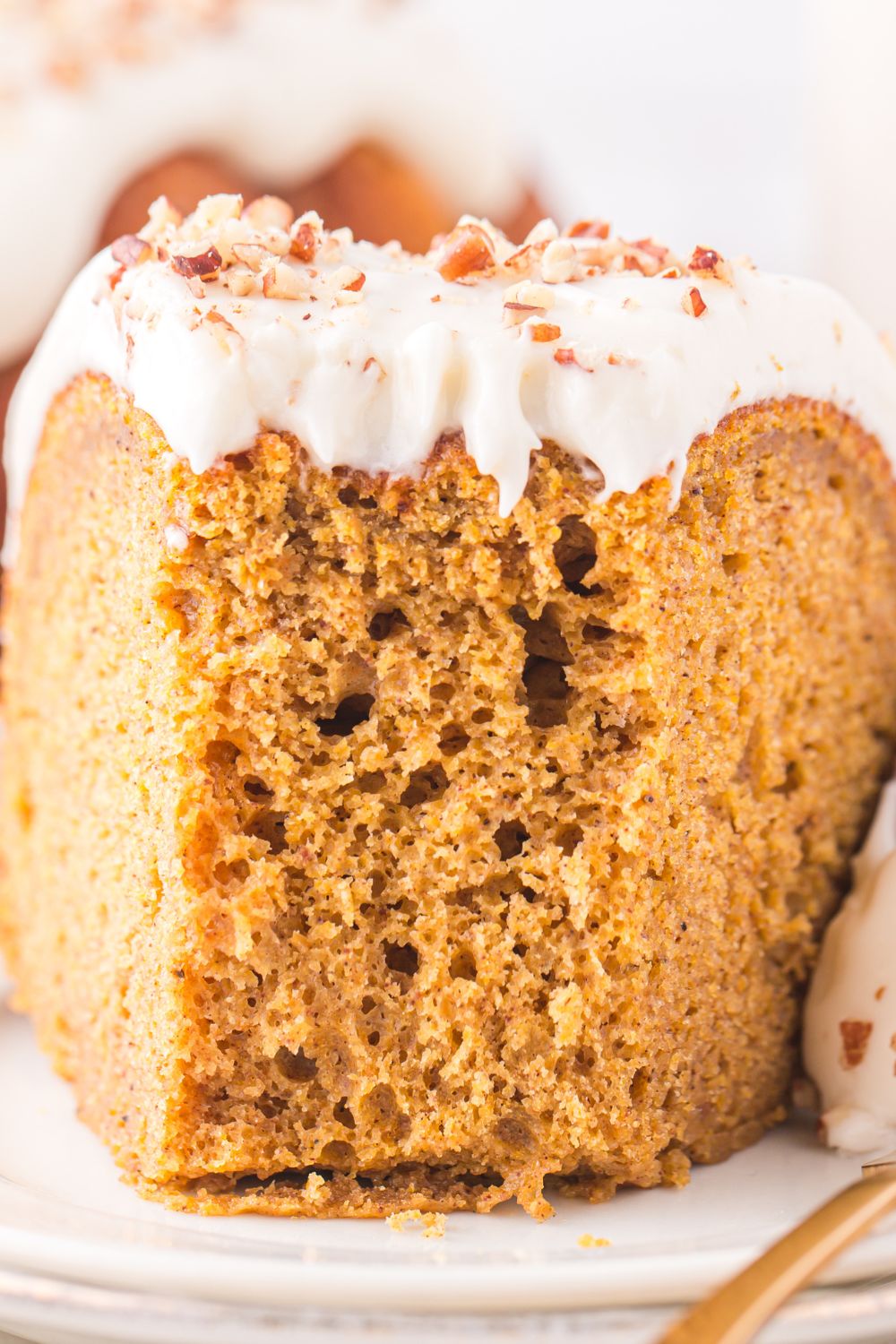 thick slice of a pumpkin bundt cake sitting on a white plate with a few bites taken out of it 