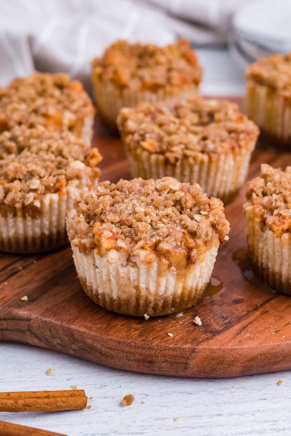 marble counter with around wooden cutting board with Apple Crisp Cheesecake Bites placed all over board with some drizzle of caramel all over the cheesecakes