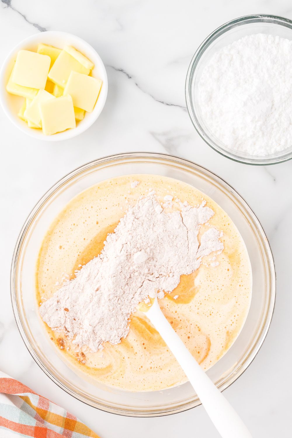 mixing up Pumpkin Cake Roll batter in a glass bowl on marble counter with butter and powdered sugar in smaller bowls to the side 