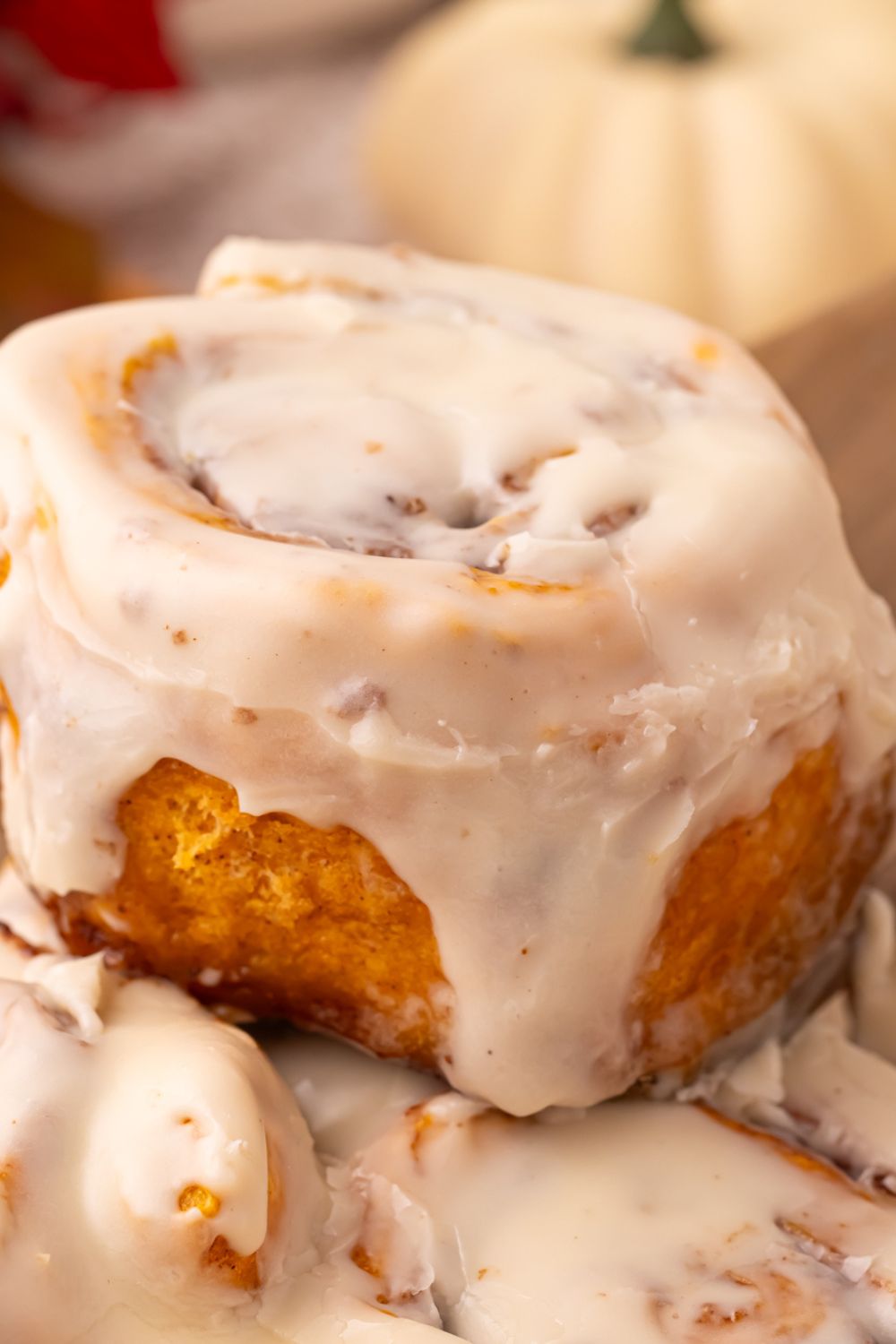 close up of Pumpkin Cinnamon Roll being lifted out of pan with glaze drizzling down the side of roll
