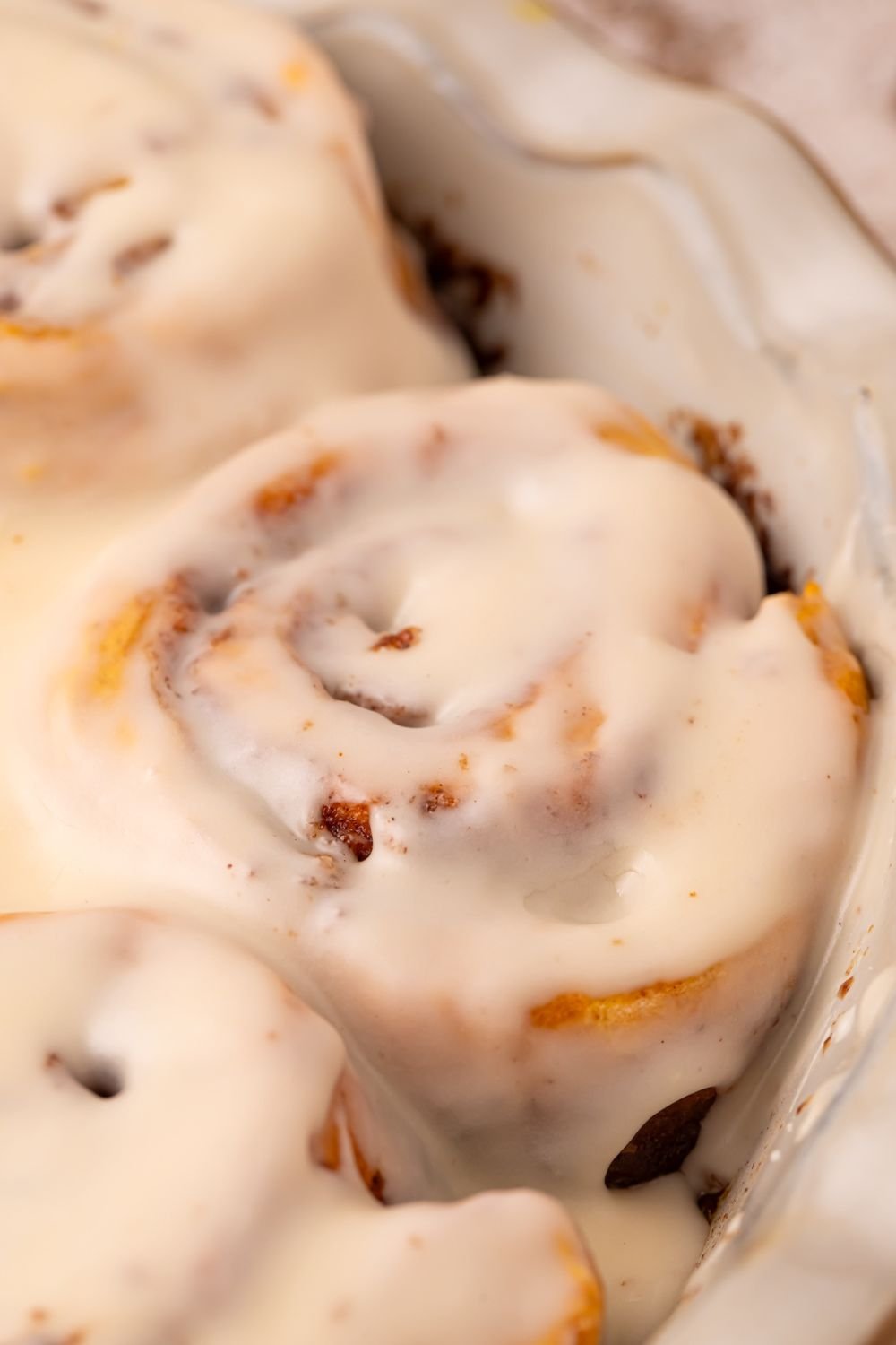 close up of Pumpkin Cinnamon Rolls in a pan on a cream colored table 