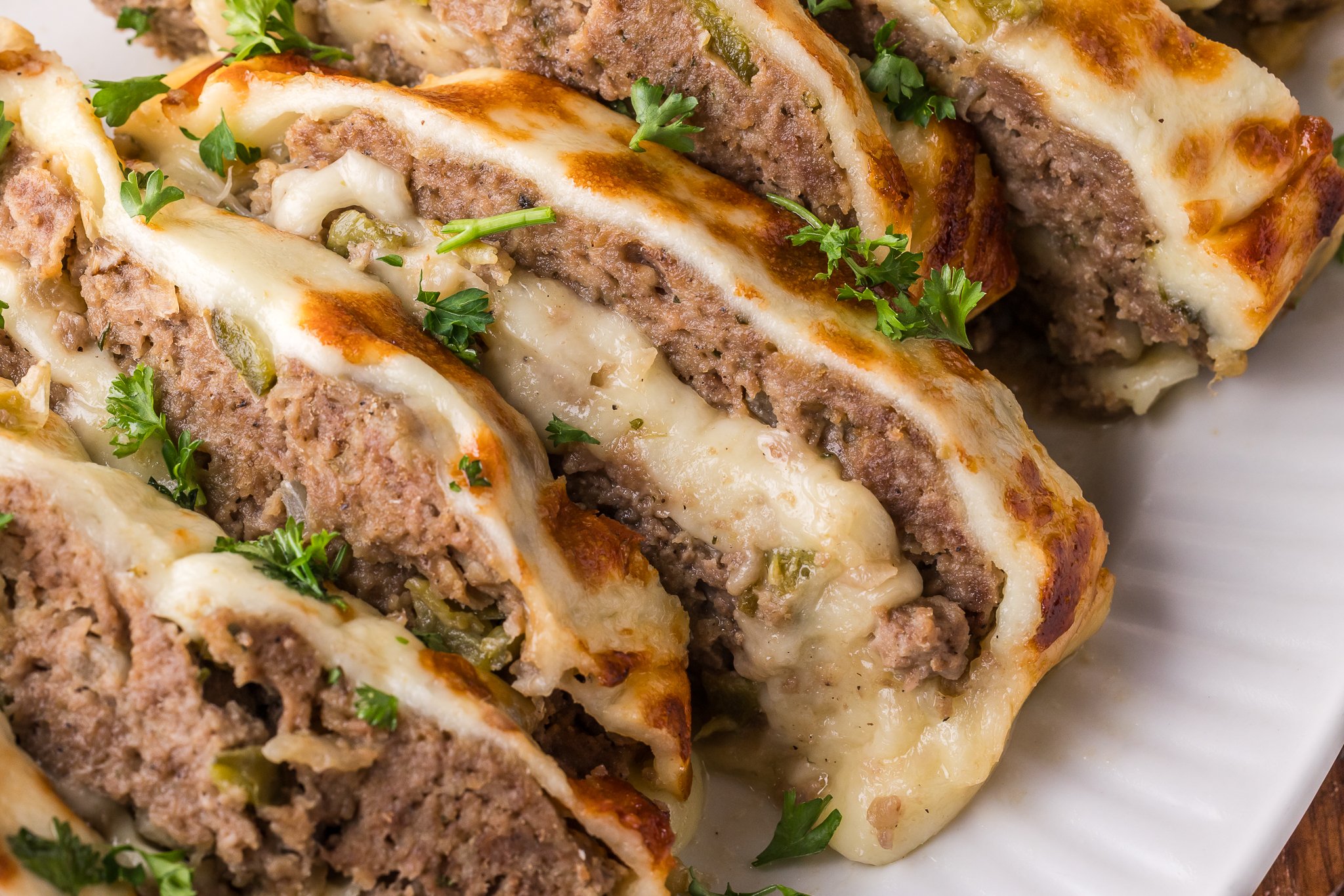 zoomed in shot of the Philly Cheesesteak Meatloaf sliced on a white serving plate showing the inside with melty cheese 