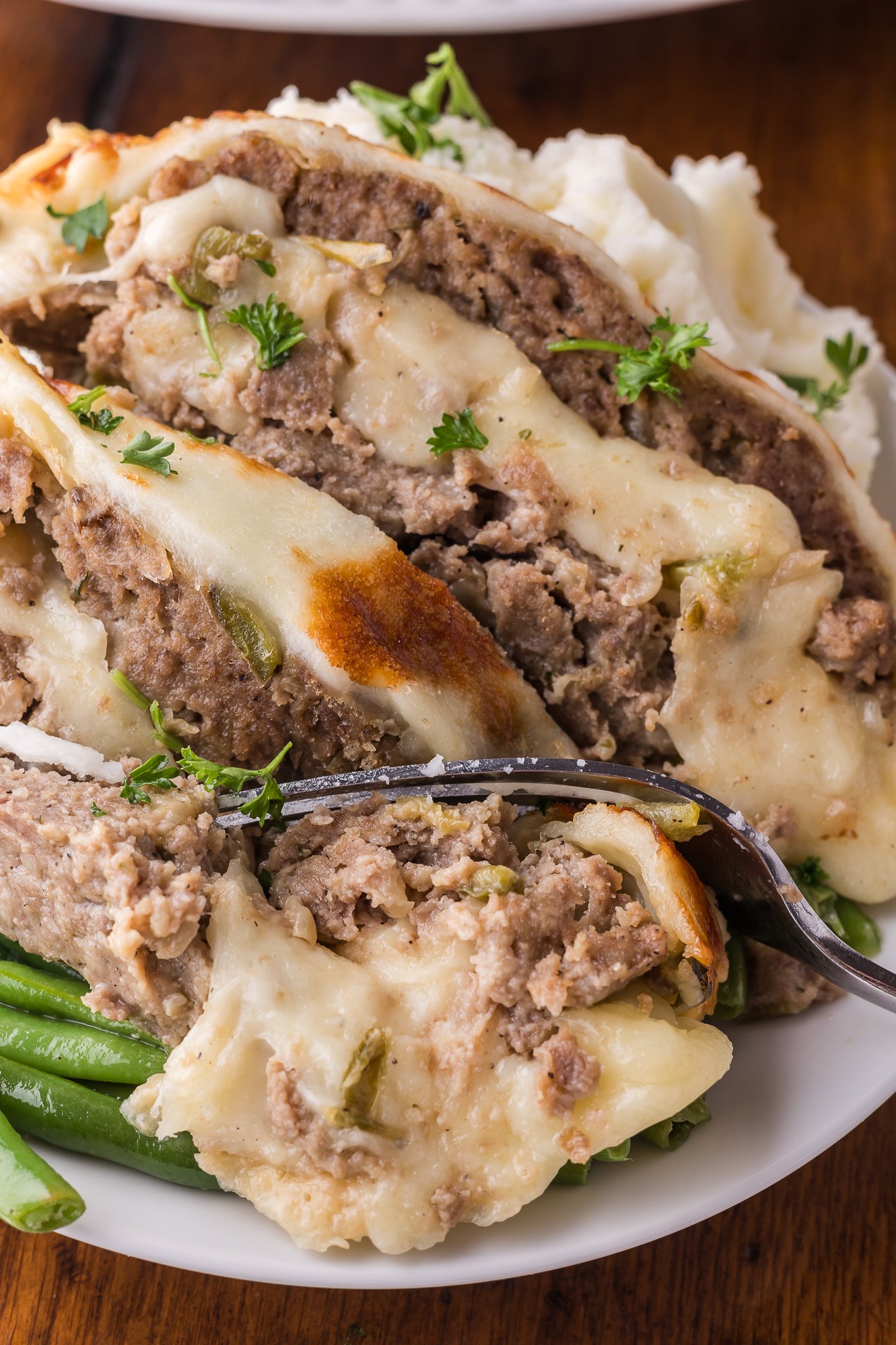 Up close shot of the Philly Cheesesteak Meatloaf sliced on a white serving plate with a fork taking out a bite