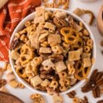 Pumpkin Spice Chex Mix in a white bowl on table with more mix scattered on table with a towel to the side of the bowl