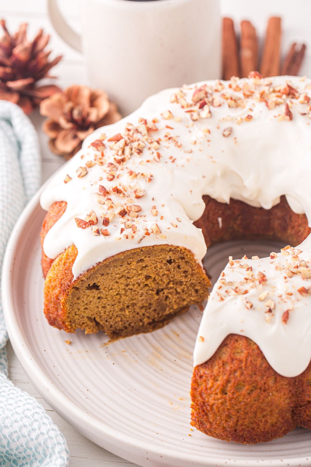 Pumpkin Bundt Cake on a white platter that has a few slices cut out and fall decor behind it 