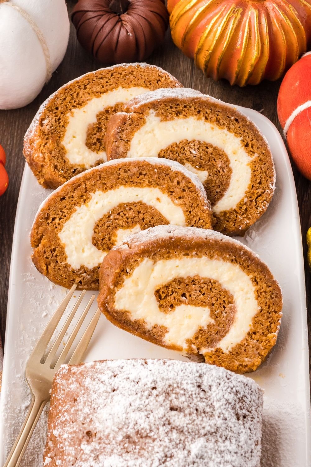 Pumpkin Cake Roll sliced and placed on a platter, and faux pumpkins around the platter for a fall themed rustic look