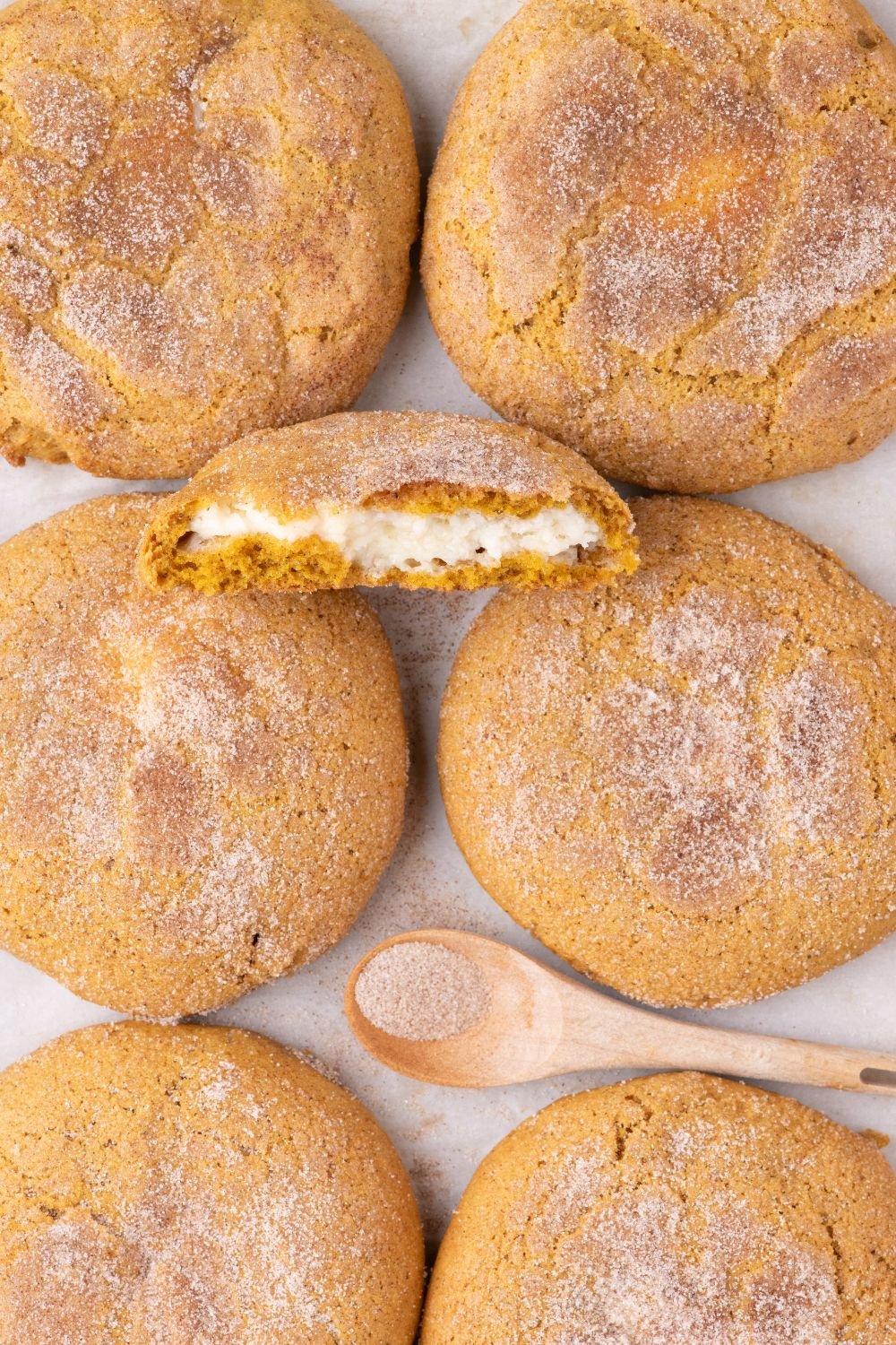 Pumpkin Cheesecake Cookies placed on table with one cookie cut in half and a spoon of cinnamon and sugar