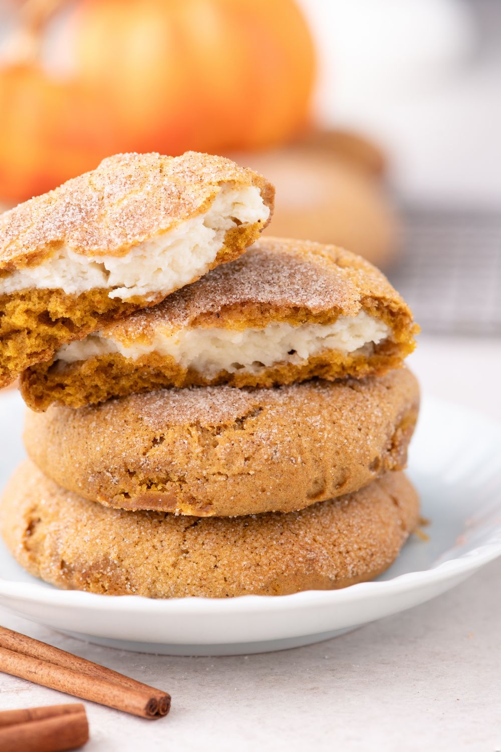 white plate with a stack of Pumpkin Cheesecake Cookies on table with one cookie cut in half