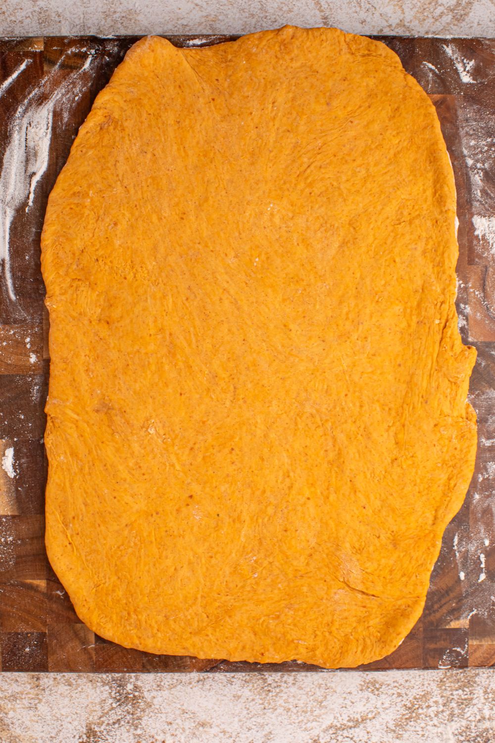 rolled out pumpkin cinnamon roll dough on wooden cutting board 