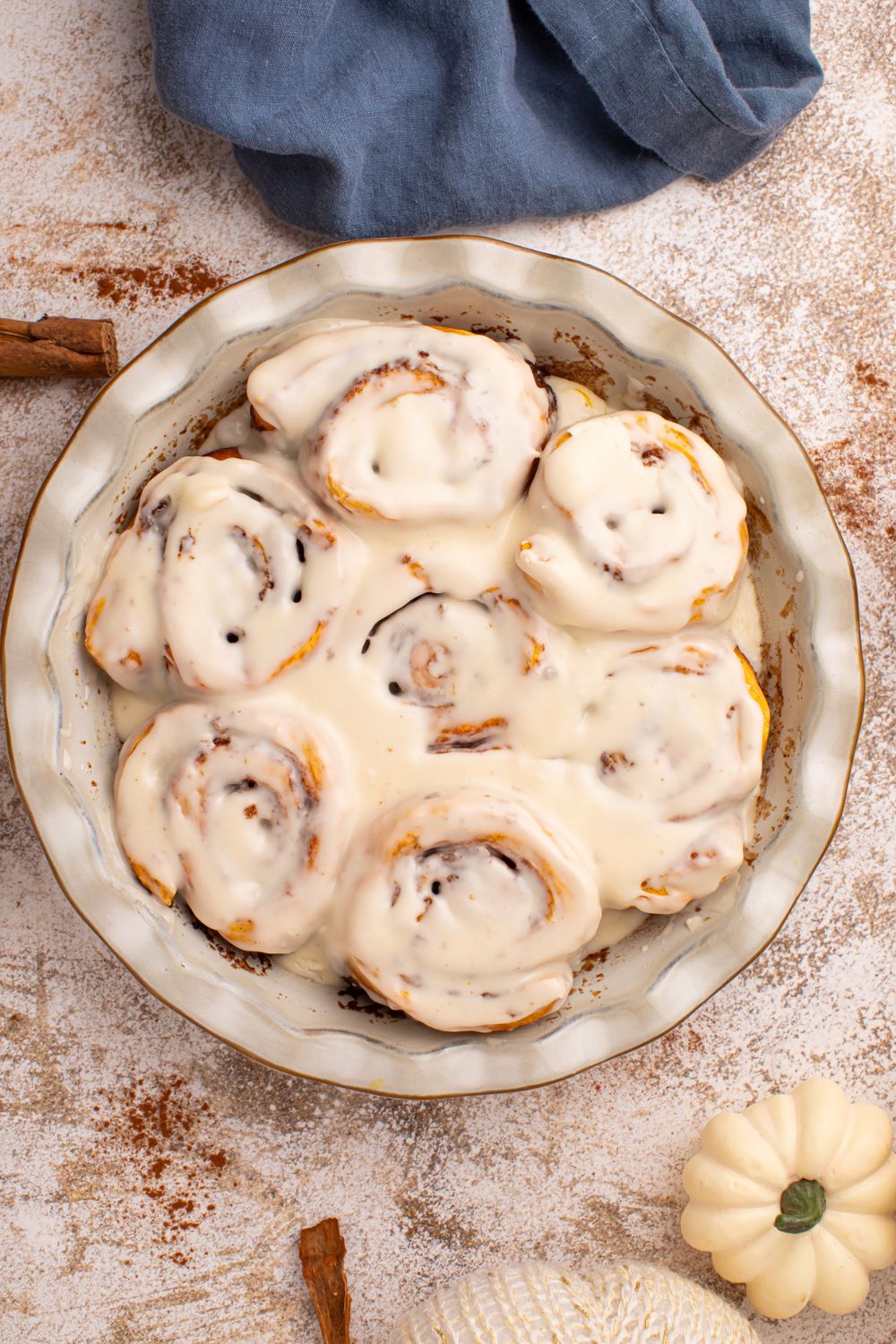 Pumpkin Cinnamon Rolls in a round dish on table with cinnamon sticks and tiny pumpkins around the table to have a fall vibe 