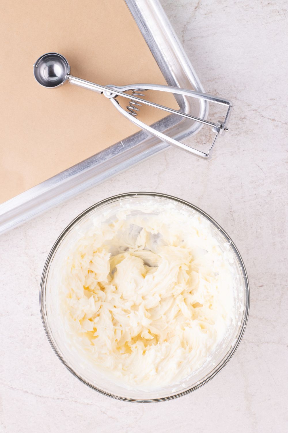 cheesecake batter in a glass bowl with a cookie sheet to side and cookie scoop