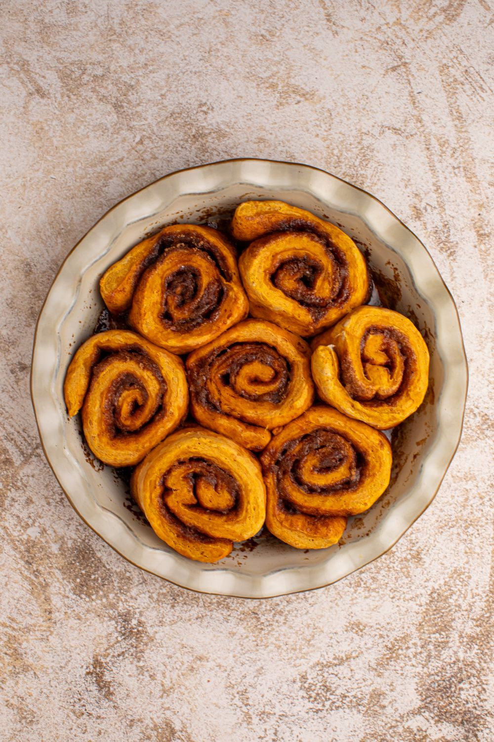 baked Pumpkin Cinnamon Rolls in a pie plate sitting on counter 