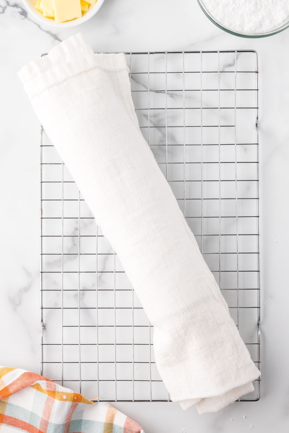 Pumpkin Cake Roll wrapped up in a white towel on a cooling rack on a marble counter 