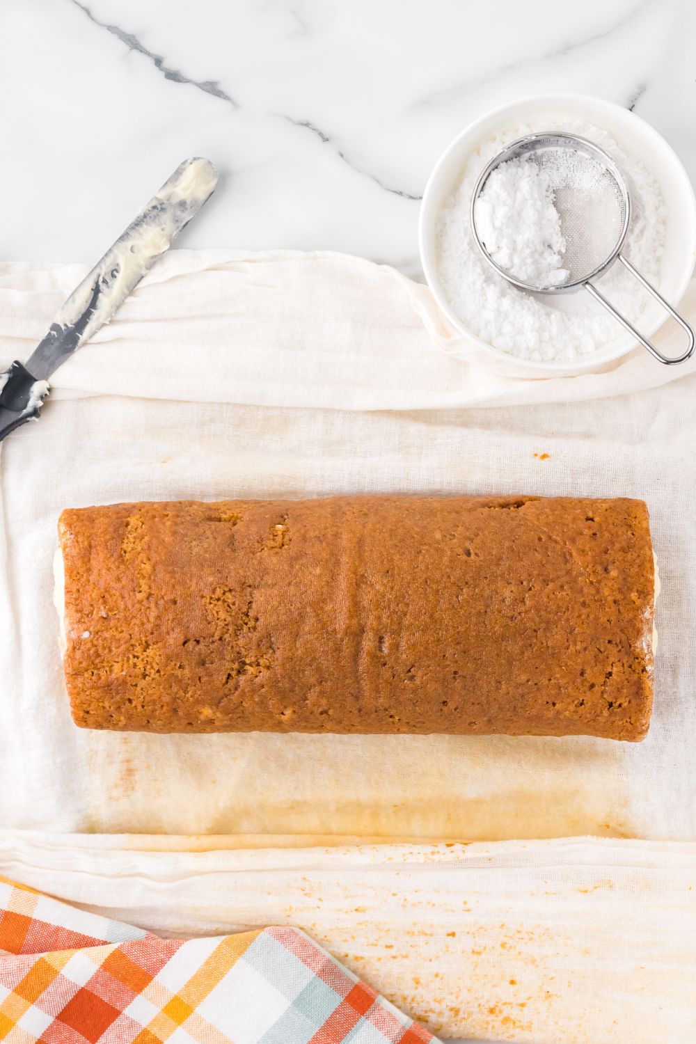 Pumpkin Cake Roll being rolled up with parchment paper under the pumpkin cake 