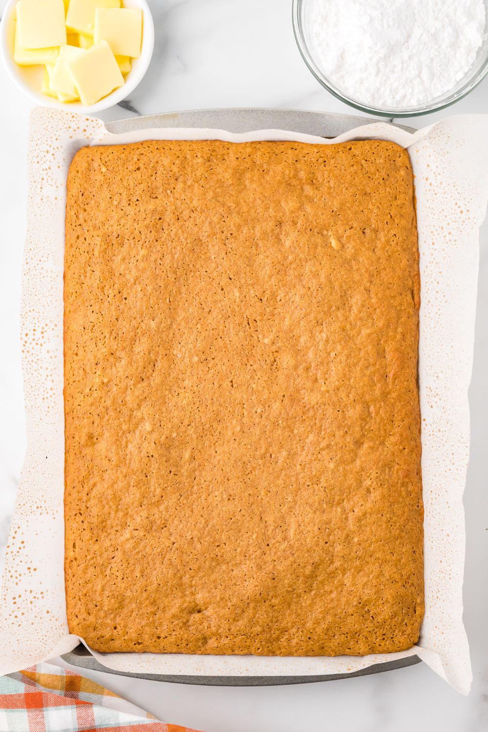 baked Pumpkin Cake Roll in a sheet pan sitting on a marble countertop 
