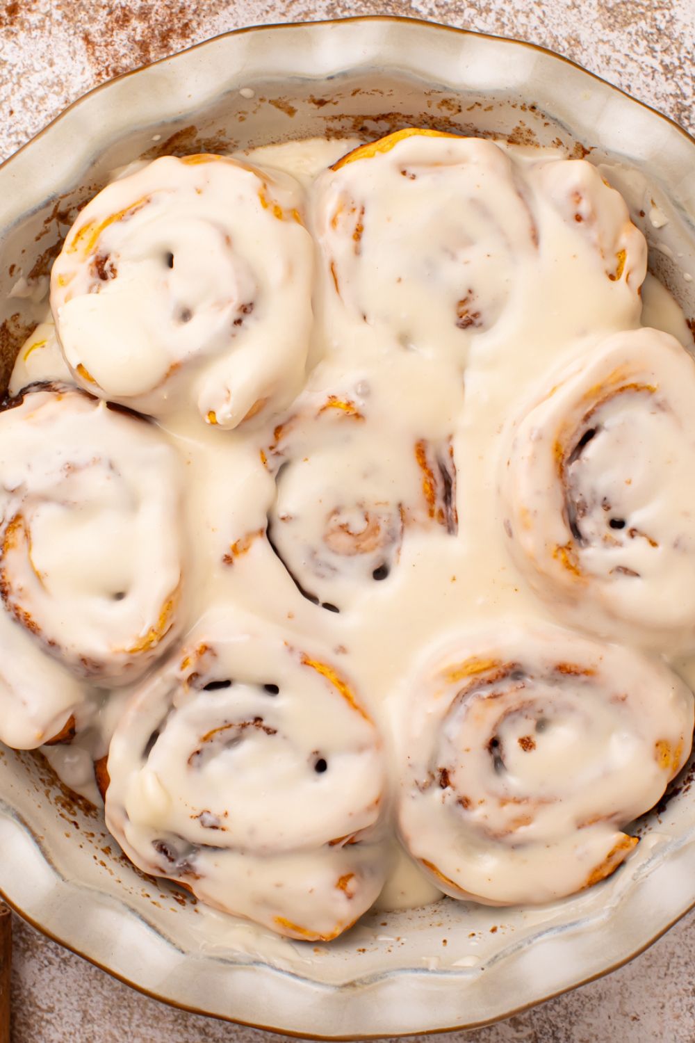 looking down at table to a round pie plate full of baked and glazed Pumpkin Cinnamon Rolls on  the table 