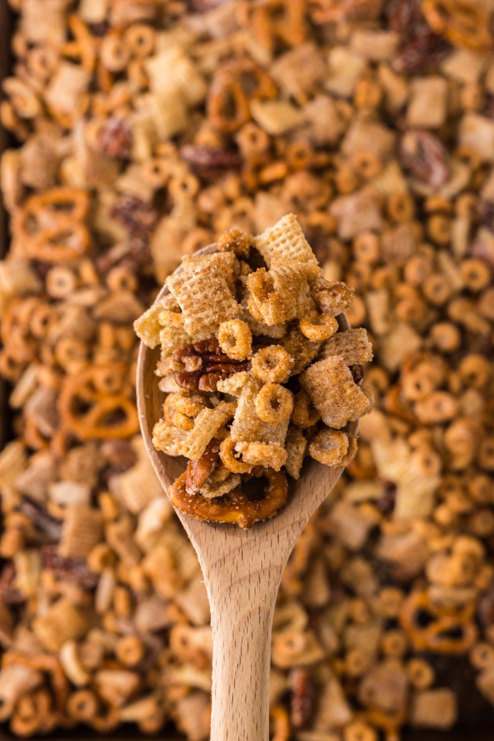Pumpkin Spice Chex Mix spread out in a pan with a wooden spoon above the table with a bunch of snack mix in it 