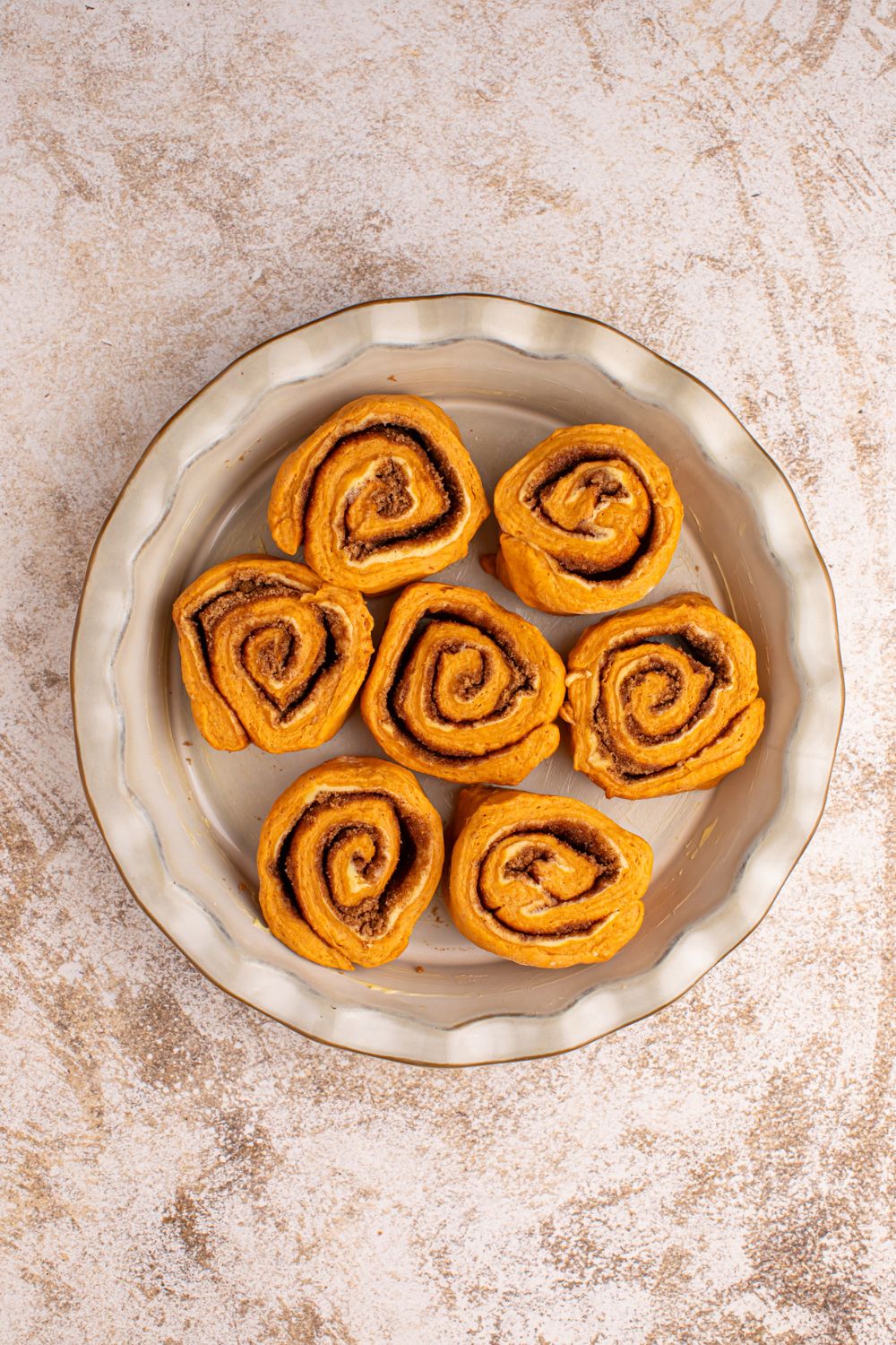 raw Pumpkin Cinnamon Rolls in a pie plate on counter 
