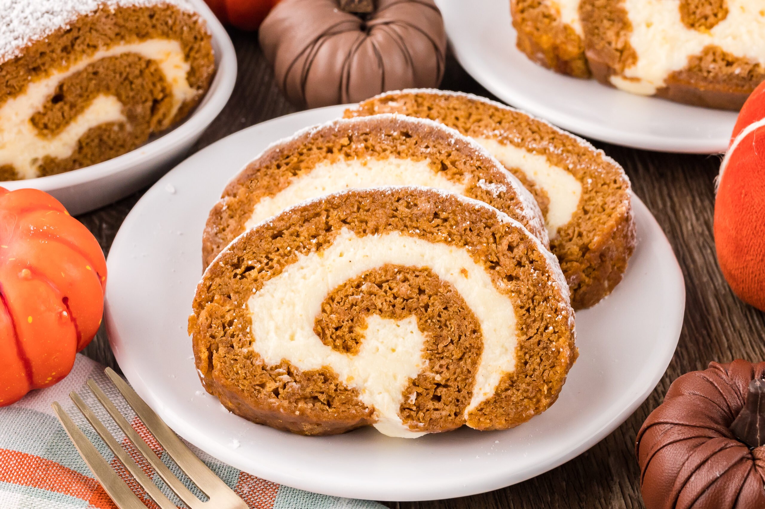 Pumpkin Cake Roll slice on a white plate on top of a dark wood table 