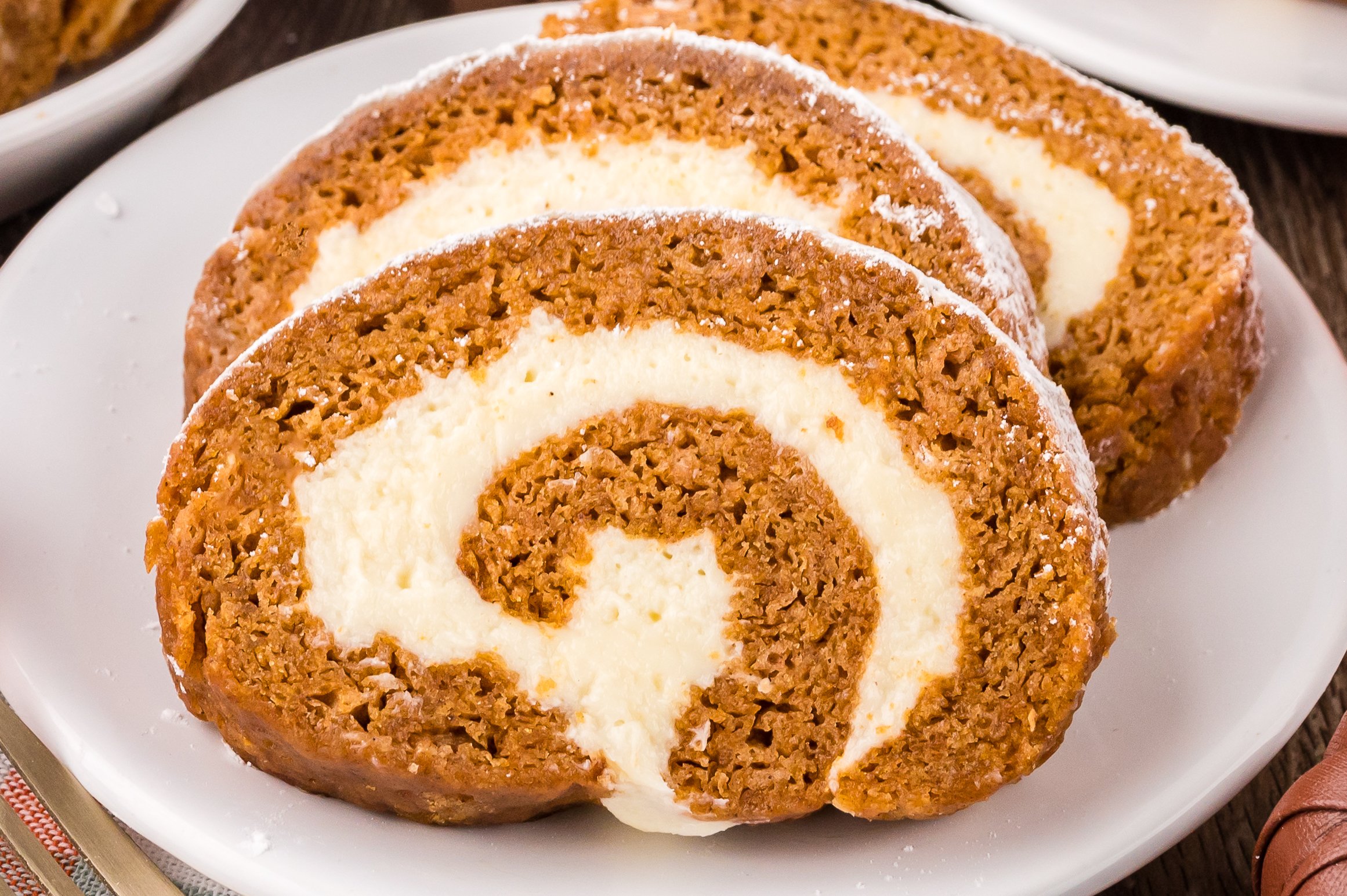 Pumpkin Cake Roll sliced on white plates placed on table with a few faux pumpkins around