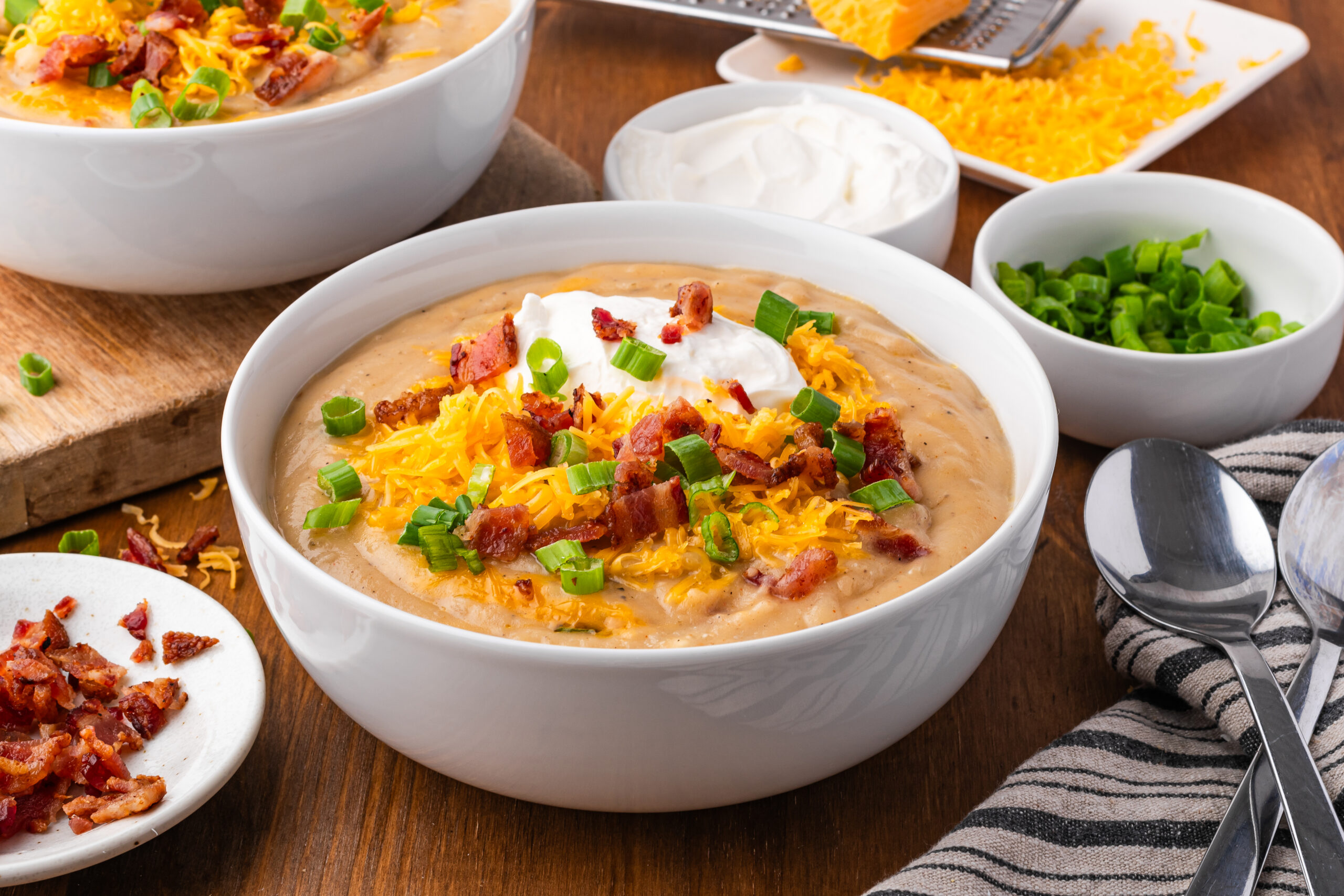 Crock pot loaded baked potato soup in a white bowl on a dark wood table 